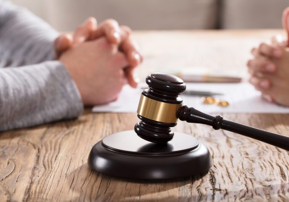 Gavel In Front Of Couple's Hand On Wooden Table